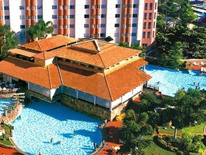 Un hôtel doté de plusieurs piscines, un grand bâtiment avec un toit en tuiles et entouré de verdure.