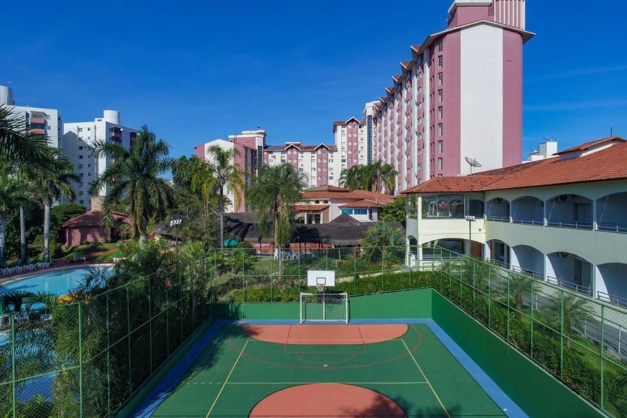 A basketball court with a net, surrounded by a fence, and adjacent to a swimming pool.