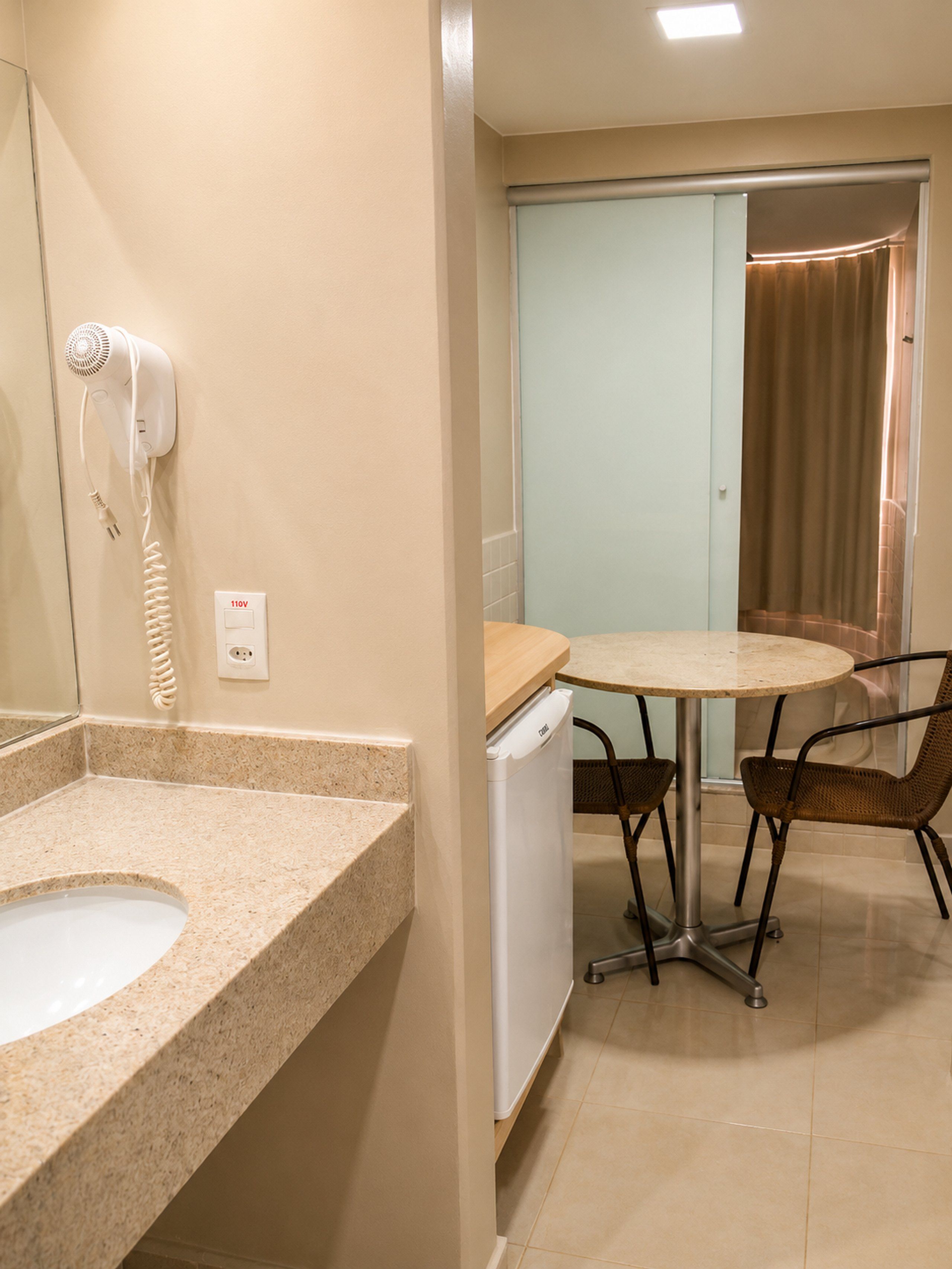 A bathroom with a sink, a hairdryer, and a small table with chairs.