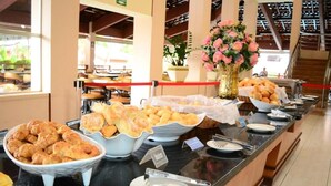 A buffet setup with various baked goods and a flower arrangement. - Hotel Maravilhoso-Banheira-PiscinaTermal (Caldas Novas)