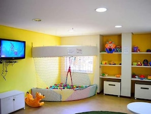 Un espace de jeux avec une piscine à balles, un téléviseur et des étagères remplies de jouets.