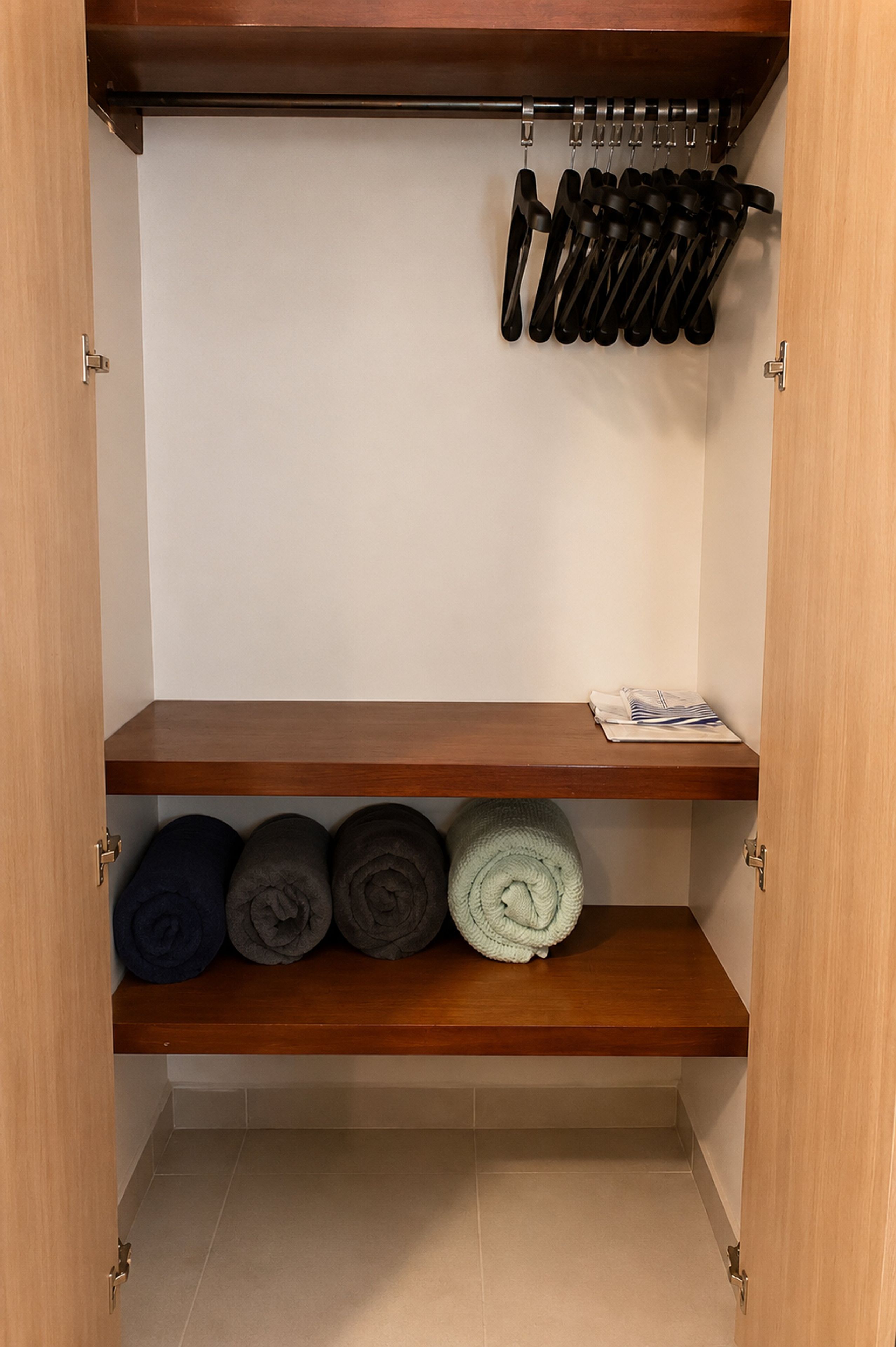 A wardrobe with shelves holding rolled towels and a rack with black kitchen utensils.