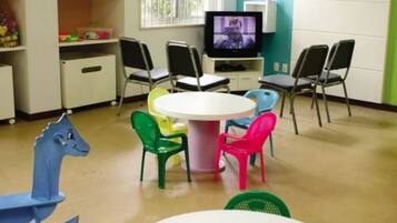 A children's playroom with a round table, colorful chairs, a television, and shelves with toys.