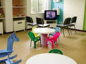 A children's playroom with a round table, colorful chairs, a television, and shelves with toys. - Hotel Maravilhoso-Banheira-PiscinaTermal (Caldas Novas)