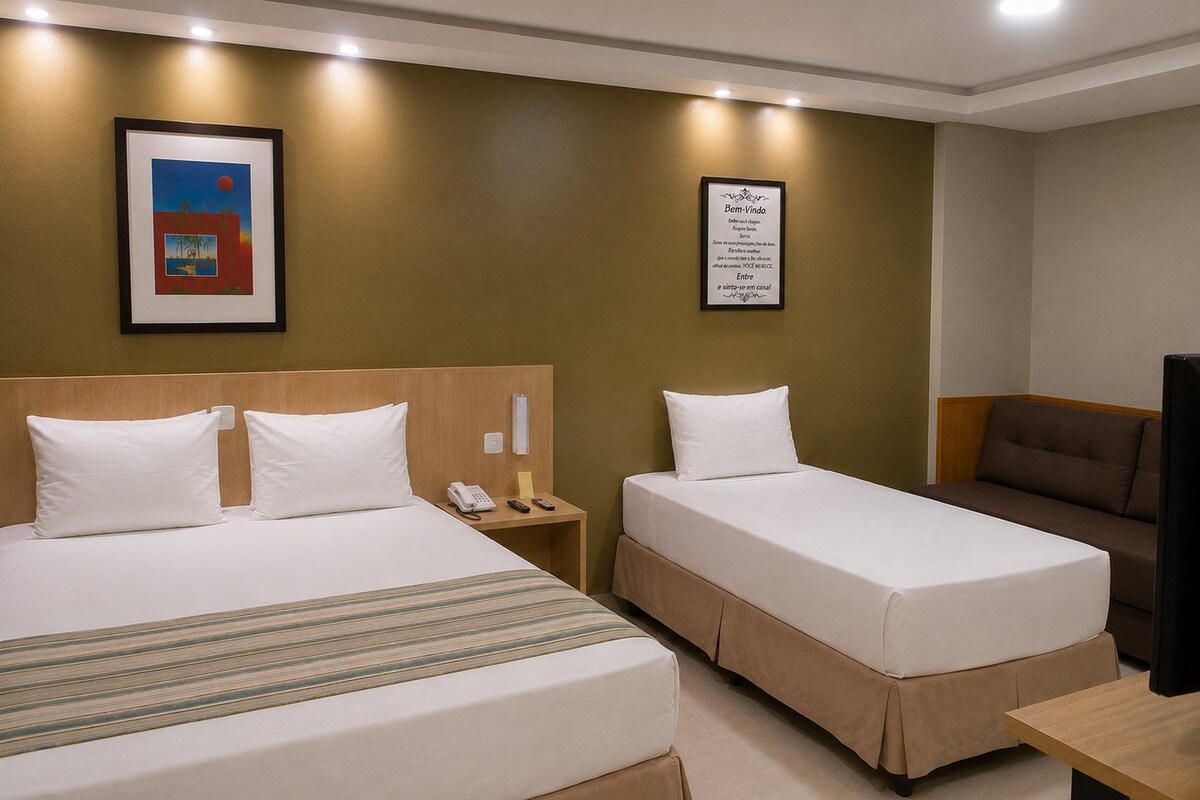 A hotel room with two beds, a desk, a TV, a phone, and a framed quote on the wall.