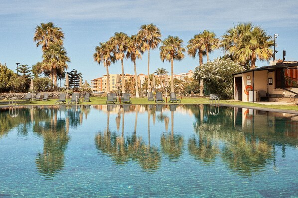 A clear pool with reflections of palm trees and a building in the background.