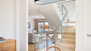 Una sala de estar moderna con una escalera de cristal, un comedor con una mesa y sillas de madera, y vistas a un balcón con sofá.