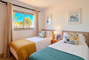 A hotel room with two beds, a window with curtains, a nightstand with a lamp, and wall art.