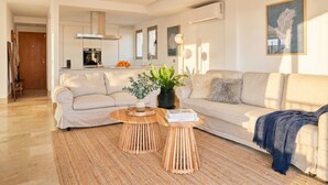 Una sala de estar moderna con un sofá, dos mesas auxiliares de madera, una planta en maceta y una estantería.
