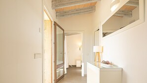 A hallway with a glass door, a white cabinet with a lamp, and a mirror on the wall.