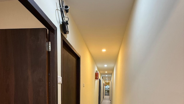 A hallway with wooden doors on the left, a covered object on the right, and a ceiling-mounted device. - Hotel Marine Line (Mumbai)