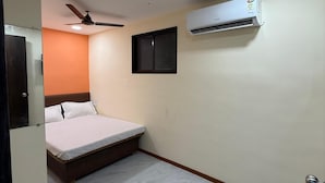 A bedroom with a bed, an air conditioner, a ceiling fan, and a small window. - Hotel Marine Line (Mumbai)