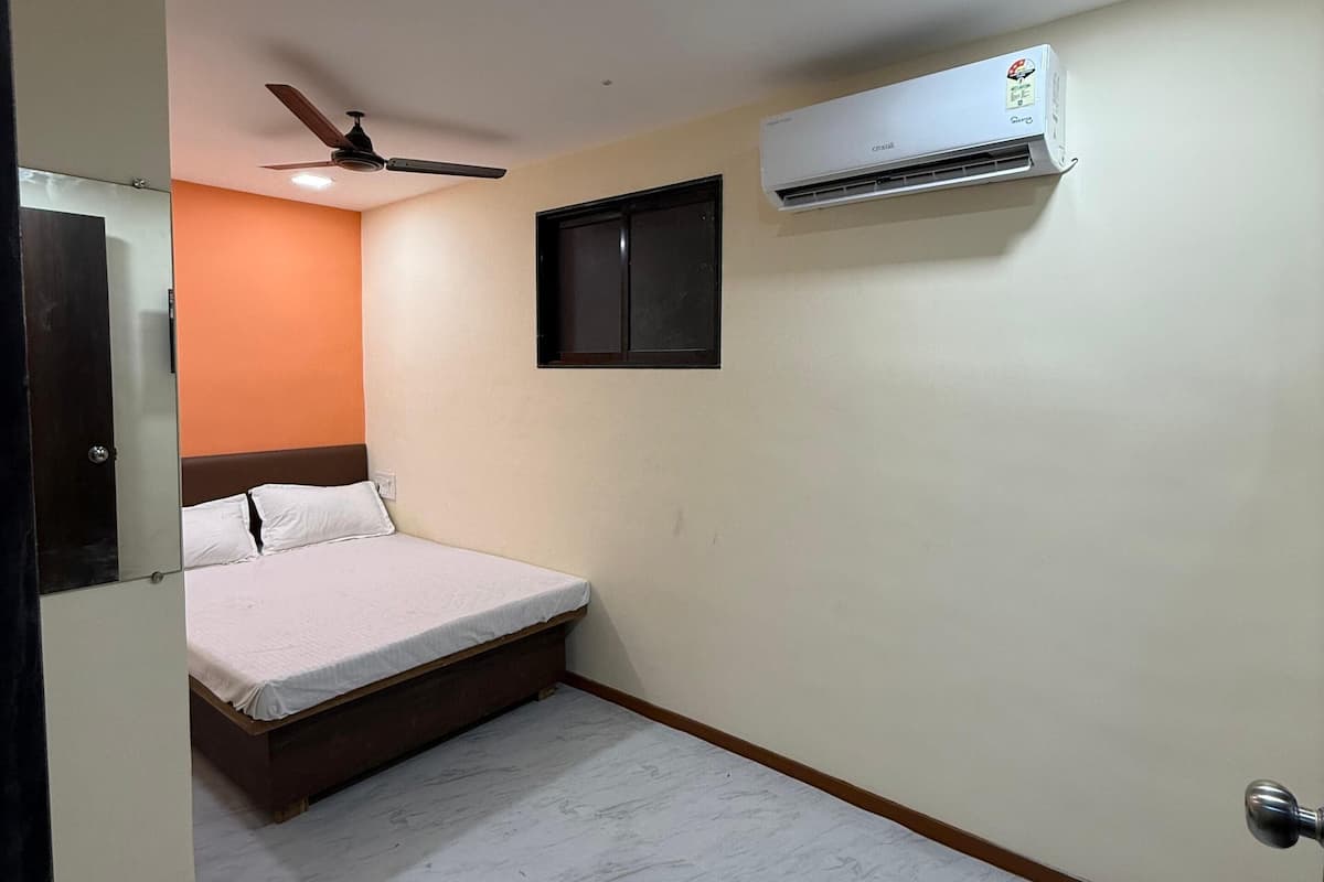 A bedroom with a bed, an air conditioner, a ceiling fan, and a small window.