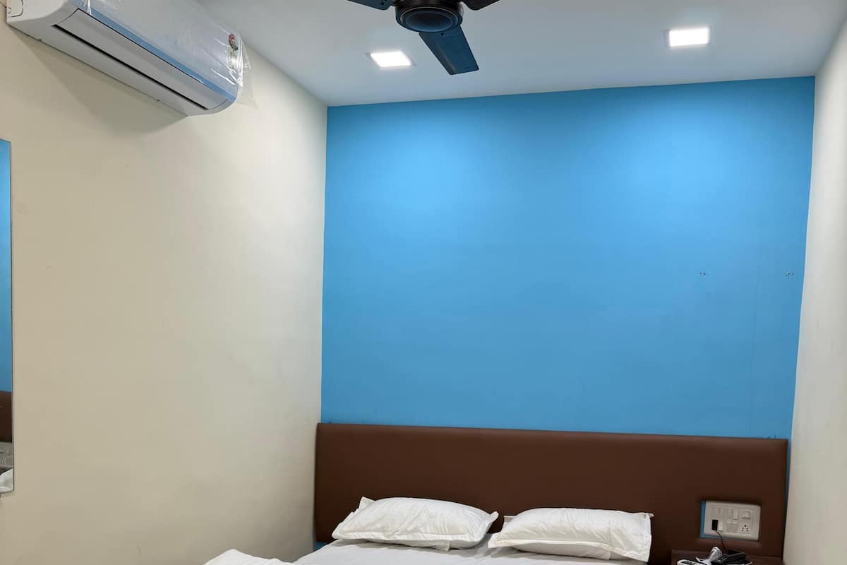 A hotel room with a bed, a ceiling fan, an air conditioner, a nightstand, and a wall socket.