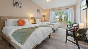 Une chambre d’hôtel avec deux lits, un ventilateur de plafond, un bureau avec une chaise et une grande fenêtre avec des rideaux.
