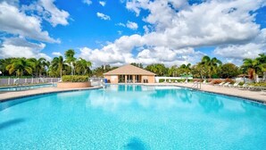 Une grande piscine à l’eau d’un bleu limpide, entourée de palmiers et bordée d’un bâtiment doté d’un toit plat.