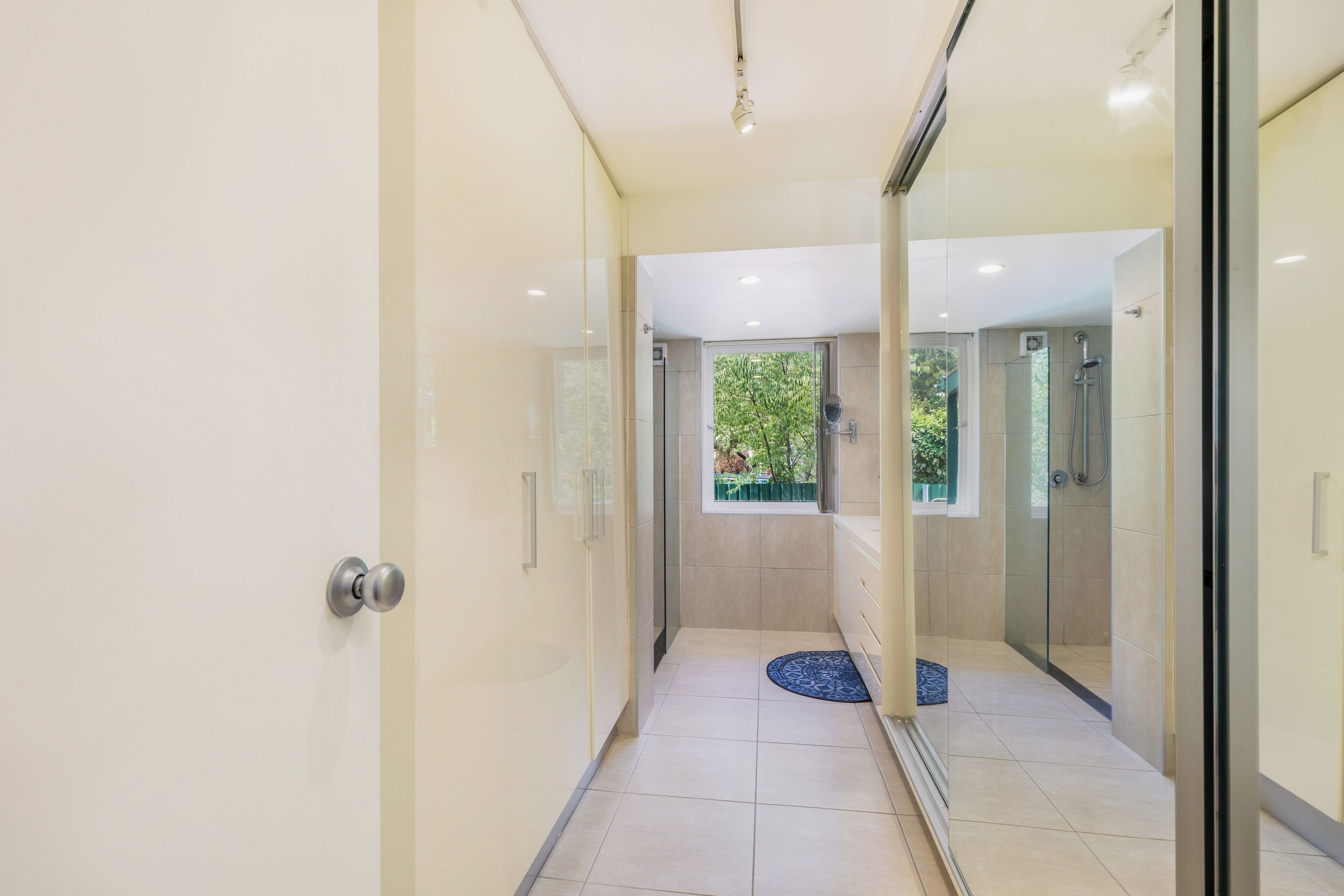 A modern bathroom with a glass shower enclosure, a visible window, and a blue mat on the floor.
