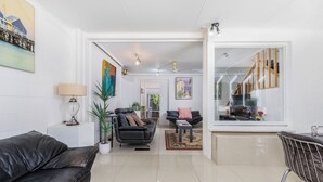 A modern living room with a black leather sofa, a glass coffee table, and a dining area with a metal chair. - Architectural Comfy 2B&2B suite with garden view close to lake & Shopping Centre (Yarralumla)