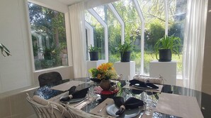 A dining area with a glass table, chairs, and potted plants. - Architectural Comfy 2B&2B suite with garden view close to lake & Shopping Centre (Yarralumla)