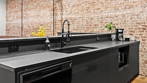 A modern kitchen with a large island, double sink, and a brick wall backdrop.