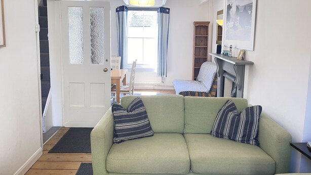 A living room with a green sofa, a fireplace, a bookshelf, and a dining area with a table and chairs.