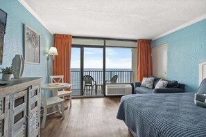 Ein Zimmer mit Bett, einer Couch, einem kleinen Tisch und Stühlen. Ein Balkon bietet Blick auf das Meer.