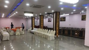 Un'ampia sala con file di sedie e tavoli ricoperti di bianco, un lampadario e un'area buffet.
