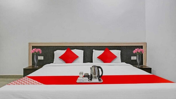 Una camera d'albergo con un letto grande, due cuscini rossi, un vassoio con una caffettiera e un vaso con fiori su entrambi i lati.
