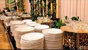 Un'area ristorazione d'hotel con piatti ordinatamente impilati e tavoli rotondi con bicchieri.