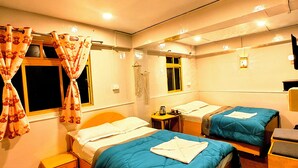 Une chambre d’hôtel avec deux lits, une petite table, une table de chevet et une fenêtre avec des rideaux.