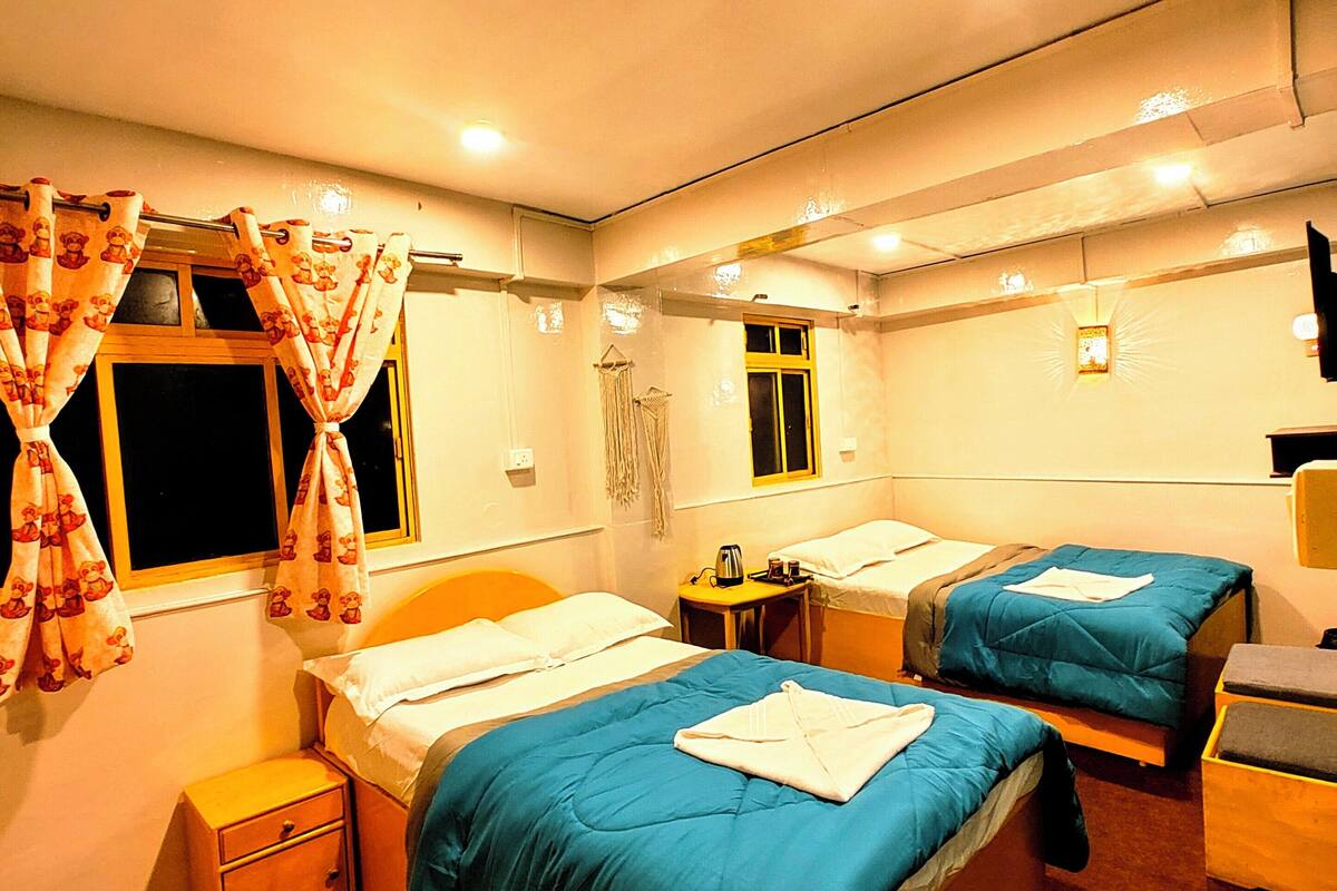 A hotel room with two beds, a small table, a nightstand, and a window with curtains.