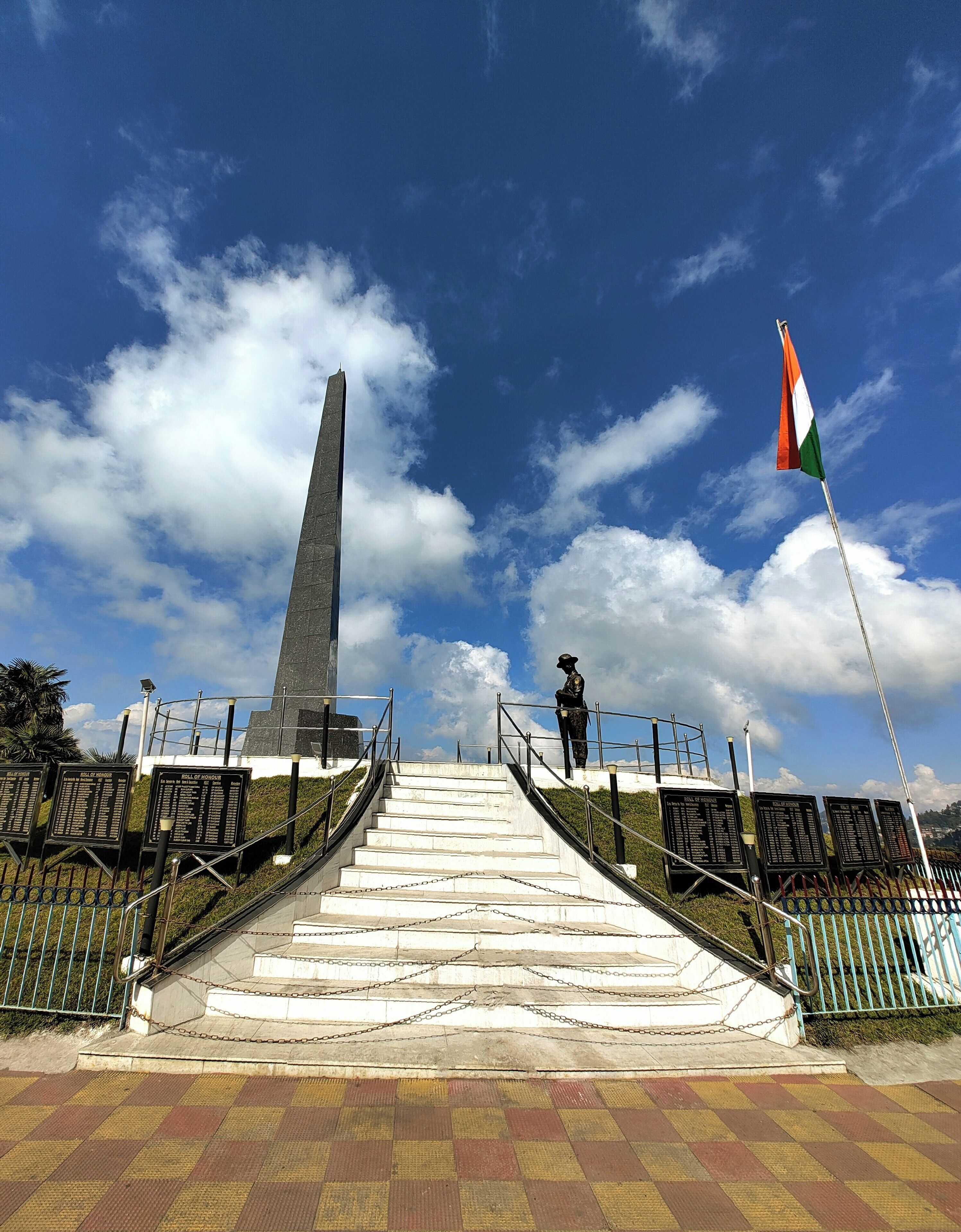 A memorial with a tall obelisk, a statue, and a flag, leading up a set of stairs.