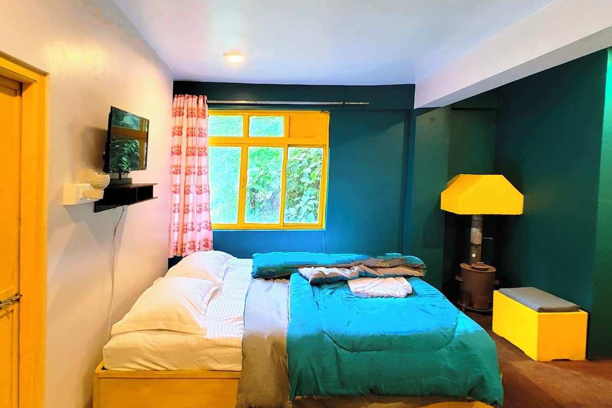 A bedroom with a bed, a window with curtains, a lamp, and a television on a shelf.