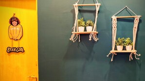 Une pièce avec une porte jaune, une étagère en macramé fixée au mur, ornée de deux plantes en pot, et une décoration murale représentant un singe portant un casque audio, avec le texte « RESTEZ ZEN ».