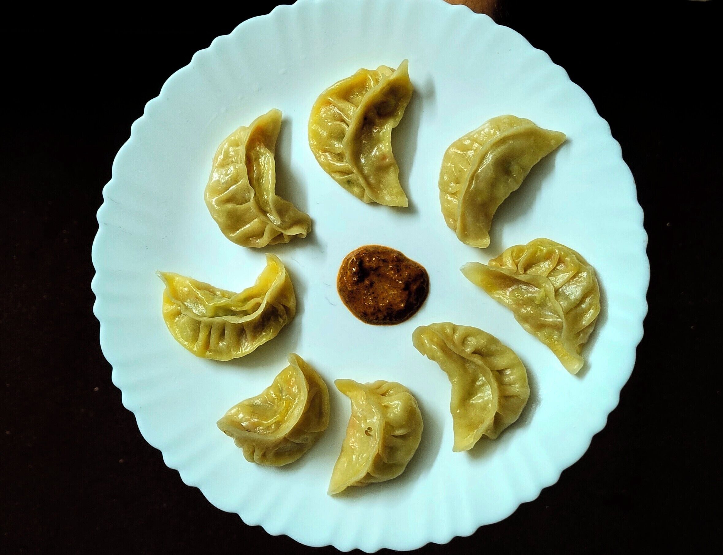 A plate of dumplings with a dark sauce in the center.