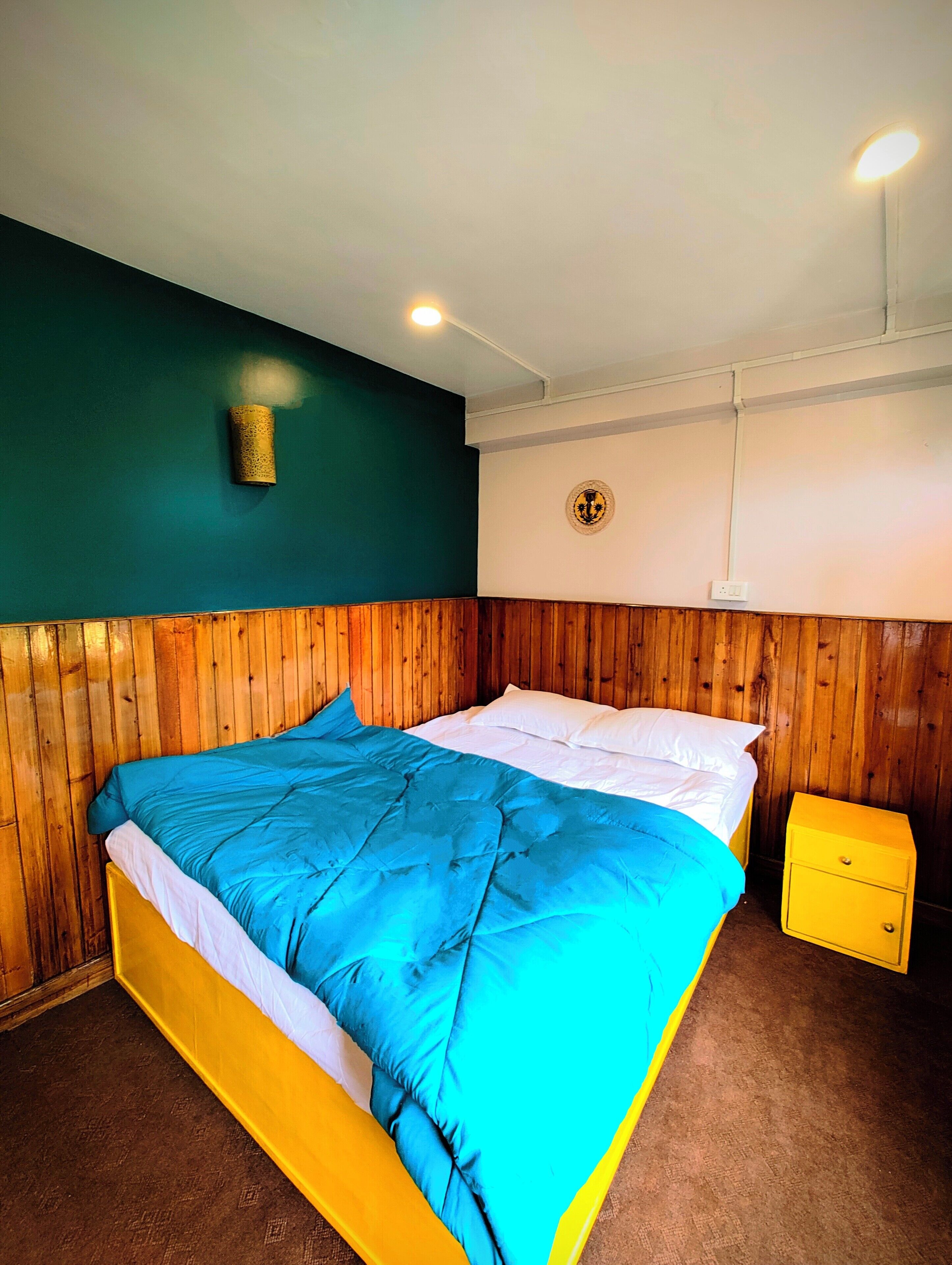 Una cama con edredón azul y blanco, cabecera de madera y mesita de noche amarilla.