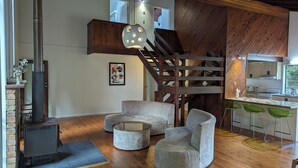 Una sala de estar moderna con chimenea, una escalera de madera y una zona de cocina.