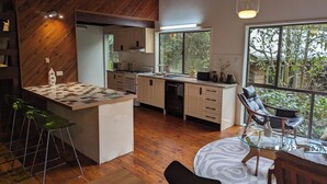 Una cocina moderna con detalles de madera, una isla central y un comedor con mesa y sillas de vidrio.