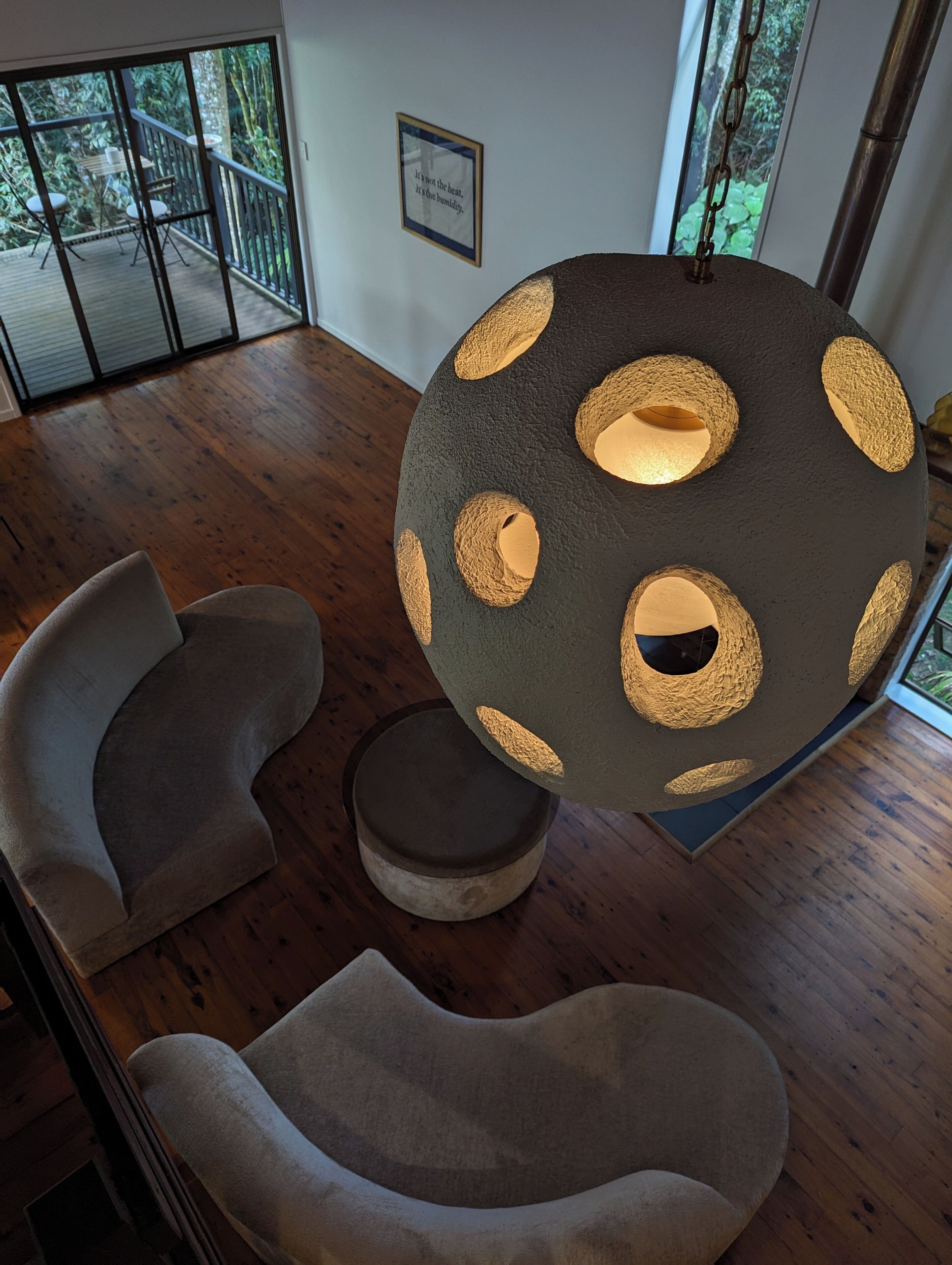 Un interior moderno con una lámpara esférica única, dos sillas contemporáneas y vistas a un balcón con terraza de madera y sillas.