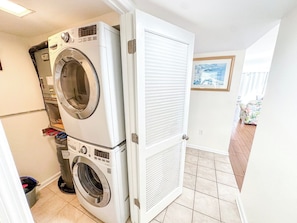 A laundry room with stacked washers and dryers, a door leading to a tiled area, and a framed picture on the wall.