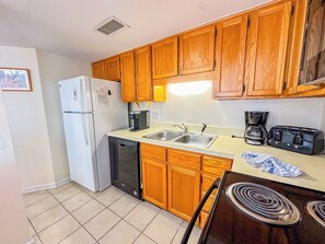 Una cocina compacta con armarios de madera, un refrigerador blanco, un lavavajillas, un fregadero y una estufa.