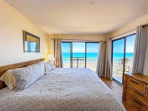 A hotel room with a large bed, a balcony with a view of the sea, and a wooden dresser.