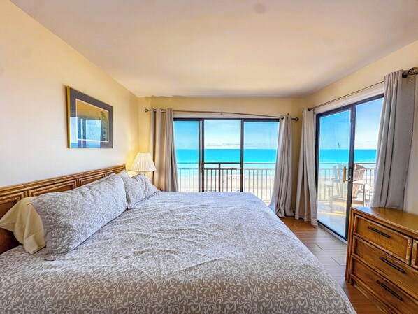 Habitación de hotel con una cama grande, un balcón con vista al mar y un aparador de madera.