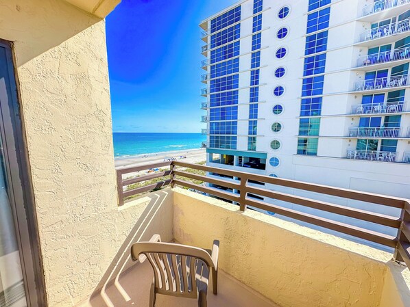 A balcony with a view of the beach and a modern building with balconies.
