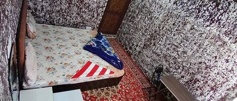 A small room with a bed, a red and white striped pillow, a blue towel, and a floral-patterned carpet.
