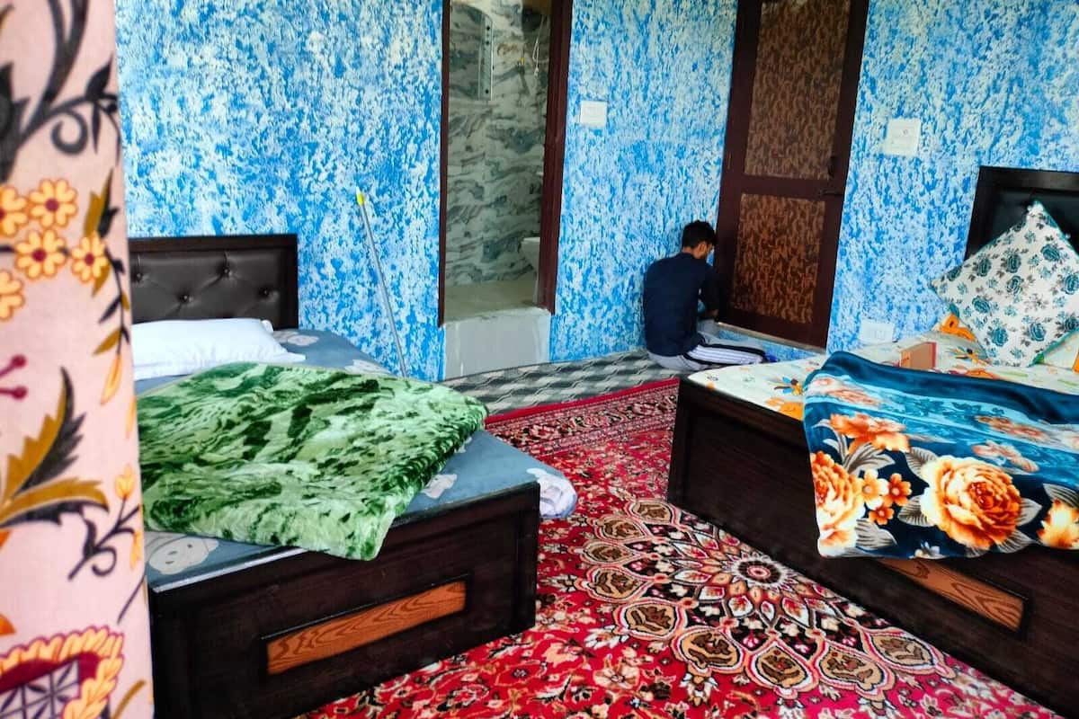 A room with two beds, a red patterned carpet, and blue floral wallpaper.