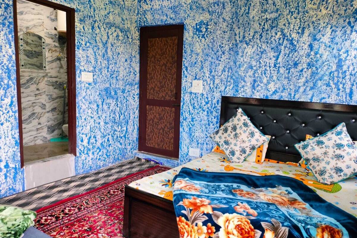 A bedroom with a bed, a nightstand, a red patterned rug, a wooden door, and a marble wall.