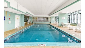 Une piscine intérieure dont la profondeur maximale est de 1,5 mètre, entourée de chaises longues et protégée par une paroi en verre.