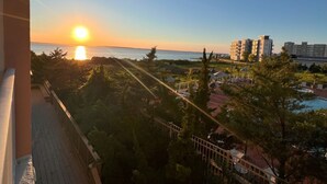 Une vue sur le coucher de soleil depuis un balcon donnant sur une piscine, avec des bâtiments en arrière-plan.