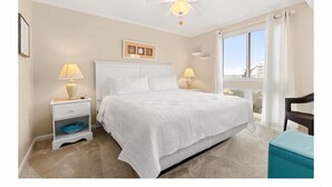 Une chambre à coucher avec un lit, des lampes de chevet, une table de chevet, un ventilateur de plafond et une fenêtre avec des rideaux.